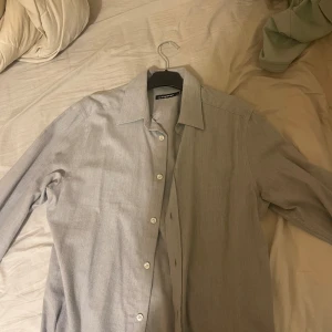 Ljusgrå skjorta från J.Lindeberg - Säljer en stilren ljusgrå skjorta från J.Lindeberg. Skjortan har klassisk krage, långa ärmar med manschett och vita knappar framtill. Materialet känns mjukt och svalt, perfekt för en clean look.