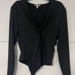 Svart omlott body med knutdetalj - Svart långärmad omlott body med snygg knutdetalj framtill. Djup v-ringning och asymmetrisk nederkant.
