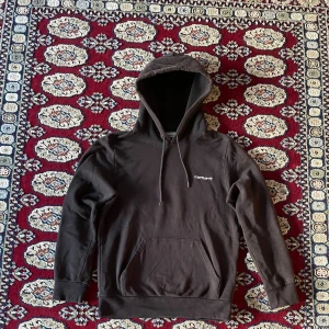 Svart Carhartt hoodie med huva - Svart hoodie från Carhartt med liten vit logga på bröstet.