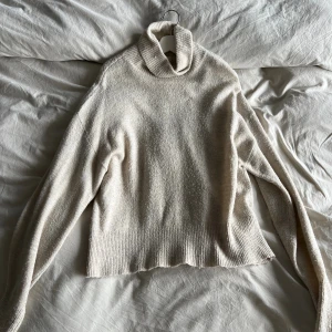 Beige polotröja i ullmix - Mysig beige polotröja med hög krage. Tröjan är stickad i ett mjukt material och har en avslappnad passform med långa ärmar. Perfekt för kyliga dagar när du vill vara både bekväm och snygg.