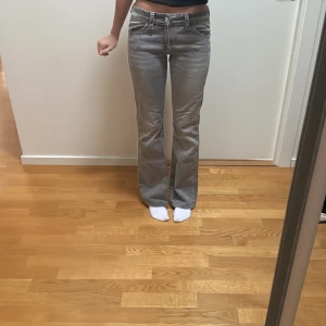 Grå bootcut jeans med broderade fickor - Snygga grå jeans med bootcut-modell och låg midja från Gina tricot. Jeansen har broderade bakfickor med knappdetaljer och klassisk femficksdesign. Tillverkade i mjukt jeanstyg med en lätt tvättad look. Nästan aldrig använda.