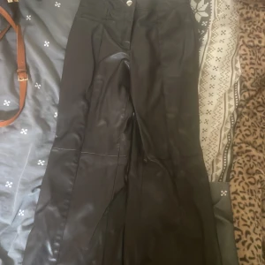 Bruna  bootcut byxor i skinnimitation H&M - Svarta byxor i skinnimitation från H&M, storlek 36. Byxorna har bootcut-modell och hög midja, med klassisk knapp och dragkedja, tyvärr har de ett hål uppe vid midjan för att jag har för stor röv 🤣