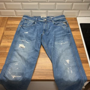 Replay Anbass Slim Fit jeans blå 32/32 - Blå jeans från Replay, modell Anbass Slim Fit. Klassisk femficksdesign med slitna detaljer och ljus tvätt. Snygga kontrastsömmar och Replay-logga på bakfickan. Tillverkade i bomull med en modern, smal passform som sitter snyggt hela vägen. ENDADST ANVÄNDA 2 GÅNGER !!! PRIS EJ HUGGET I STEN !!!!