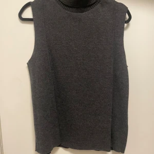Mörkgrå stickad väst från Zara - Säljer en mörkgrå stickad väst från Zara (som ej säljs längre) med hög, ribbad polokrage. Aldrig använd. 