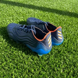 Adidas Copa Sense 1 blå fotbollsskor - Säljer ett par Adidas Copa Sense fotbollsskor i marinblått med orange detaljer och vita ränder på hälen. Skorna har snörning, vågformad design och blå sula med dobbar för gräsplan. Perfekta för dig som vill sticka ut på planen. Använt ett fåtal gånger. Nypris ca 2000