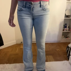Ljusblå bootcut jeans med hög midja - Säljer ett par ljusblå jeans med bootcut och hög midja. Jeansen har klassisk femficksdesign, bälteshällor och dragkedjegylf. Snygg passform som sitter tajt upptill och släpper ut vid benen. Perfekta för dig som gillar en trendig och bekväm stil.