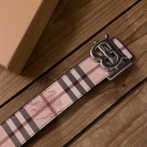 Burberry vändbart skärp med B-spänne - Säljer ett vändbart Burberry-bälte i skinn med klassiskt rutigt mönster. Ena sidan är ljusrosa med beige och bruna rutor, andra sidan är svart med mörkgrå rutor. Stort silvrigt B-spänne framtill. Perfekt accessoar för att lyfta din outfit. Om ni har funderingar eller frågor hör av er!