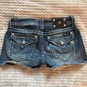 Miss Me jeansshorts med nitar - Säljer ett par blå jeansshorts från Miss Me med coola nitar och quiltad look framtill. Shortsen har råa kanter, snygga bakfickor med detaljer och silverfärgade knappar. Perfekta för dig som vill sticka ut i sommar!