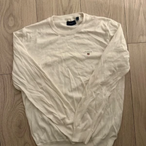 Vit bomullströja från GANT - Klassisk vit tröja från GANT i mjuk bomull. Tröjan har rund halsringning, långa ärmar och en liten broderad GANT-logga på bröstet. Perfekt för en clean och stilren look. Behöver bara strykas.