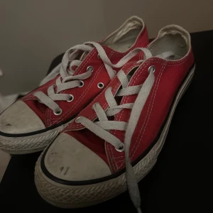 Röda Converse All Star sneakers - Klassiska röda Converse All Star sneakers med vit sula och vita snören. Skorna har rund tå, platt sula och tydliga vita sömmar. Tillverkade i textil med metallöljetter för snörningen. Perfekta för en cool och avslappnad stil. Dessa är vintage.