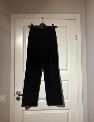 Svarta kostymbyxor med raka ben - Snygga svarta kostymbyxor med hög midja och raka, vida ben. Klassisk design med bälteshällor, knapp och dragkedja framtill samt diskreta bakfickor. Perfekta för en clean och stilren look. Materialet känns mjukt och har en lätt stretch.