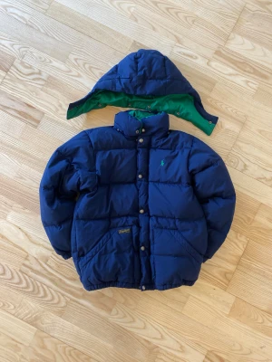 Blå pufferjacka från Polo Ralph Lauren - En extremt varm och bekväm pufferjacka för vintern nu när det nörjar bli kallt. Den är original och i jättefint skick. Det är bara en liten tygbit på insidan (se bilder) som är lös. Passar förmodligen folk mellan 150-165. Storlek: 10-12/M. Kom med bud 🙌