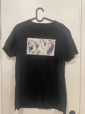 Svart Limitato t-shirt med print - Har små håll vid magen inte så synligt.   Svart t-shirt från Limitato med rund hals och korta ärmar. På bröstet finns ett rektangulärt vitt print med konstnärligt mönster i mörkblått. T-shirten är gjord i mjuk bomull och har en clean, modern vibe som passar till jeans eller shorts.