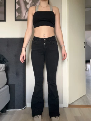 Svarta bootcut jeans med hög midja - Säljer ett par svarta jeans med bootcut och hög midja. Byxorna har klassiska fem fickor, dragkedja och knapp framtill samt breda ben som blir vidare nedtill. Materialet är jeans och de har en stilren look som passar till sneakers eller boots.