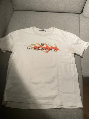 Vit Givenchy t-shirt med flames - Snygg vit t-shirt från Givenchy med coolt flames-tryck i rött, gult och svart över bröstet och Givenchy-logga. Klassisk rund hals och korta ärmar. Materialet är mjuk bomull som känns skönt mot huden. Perfekt för dig som gillar streetstyle och designer.