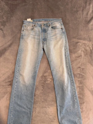 Levi's 501 ljusblå jeans W34 L34 - Ljusblå Levi's 501 jeans med klassisk femficksdesign och raka ben. Jeansen har en snygg tvättad look, bruna sömmar och ikonisk läderpatch bak i midjan. Passar dig som gillar tidlös stil och vill ha ett par jeans med autentisk vibe.