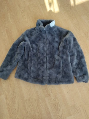 Grå pälsjacka med dragkedja - Mysig grå pälsjacka med hög krage och dragkedja framtill. Jackan har en fluffig och mjuk känsla, perfekt för kyliga dagar. Långärmad och i en enkel, stilren design som passar till det mesta.