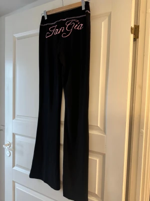 Svarta bootcut byxor från Size M - Snygga svarta bootcut byxor från IamGia med rosa broderad logga på baksidan och rosa sömdetaljer vid midjan. Byxorna har hög midja och är gjorda i ett mjukt, stretchigt material som sitter skönt och ger en cool siluett. Korea brand!