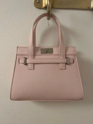 Ljusrosa handväska med axelrem - Helt ny oanvänd ljusrosa handväska med silver detaljer som även kommer med ett axelband.