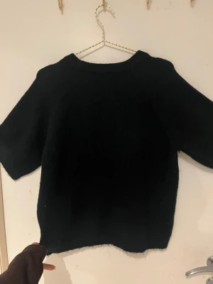 Svart stickad tröja från 157 - Svart stickad tröja från 157 med rund hals och korta ärmar. Enkel och clean design som funkar till många olika stilar. Mjuk och skön känsla tack vare det stickade materialet. Perfekt för dig som gillar minimalistiskt och klassiskt.