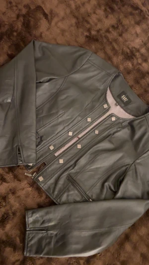 Skinnjacka från Saki  - Hej säljer en super fin skinnjacka från Saki i storlek 38 då den tyvärr inte kommer till användning. Jackan är midjekort och har fin slits vid armarna längst ner. Använd väl men i fint skick. Nypris - 1999 mitt pris -750