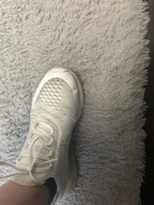 Nike Air Max 270 vita sneakers - Nike Air Max 270 sneakers i helvitt med mesh-överdel och synlig luftdämpning i hälen. Snygg sportig design med snörning och rund tå. Perfekt för dig som gillar streetstyle och vill ha bekväma skor med modern vibe.