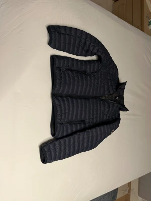 Mörkblå dunjacka från Colmar - Säljer en snygg mörkblå dunjacka från Colmar  med quiltad design och dragkedja framtill. Jackan har två praktiska sidofickor med dragkedja och en liten logotyp på ärmen. Perfekt för kyliga dagar och har en lätt, smidig passform. Mörkblå utsida, mörkgrått foder. 