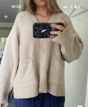 Beige oversized kofta med knappar - Säljer en beige, oversized kofta med v-ringning och stora ribbade muddar. Koftan har tre knappar framtill och två praktiska fickor. Materialet är stickat och ger en chill och mysig vibe, perfekt för lager-på-lager under kallare dagar.