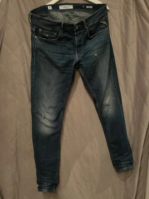 Replay willbi jeans - Snygga Replay jeans i mörkblå tvätt med slitningar och lätt distressed look. Modellen har klassisk femficksdesign, raka ben och snygga detaljer på bakfickorna. Strl W32/L34