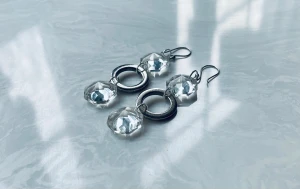 Glittriga örhängen med kristall och ring i stål - Snygga örhängen med två facetterade, klara kristaller och en rund silverfärgad ring i mitten. Hängande modell med krokar i metall. Perfekta för dig som vill sticka ut med ett coolt och glittrigt statement.