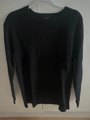 Svart stickad tröja med från H&M - En klassisk svart stickad tröja från H&M med rundad hals och långa ärmar. Tröjan har en enkel och stilren design som passar perfekt till jeans eller kjol. Perfekt för lager-på-lager och för kyligare dagar