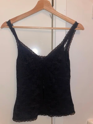 Svart spetslinne från Brandy Melville - Supersött oanvänd svart linnetopp från Brandy Melville i spets med smala axelband och liten rosett framtill. Toppen har v-ringning och fina spetsdetaljer längs kanterna. Jag har aldrig använd den!Skickar inom 1-3 dagar. 