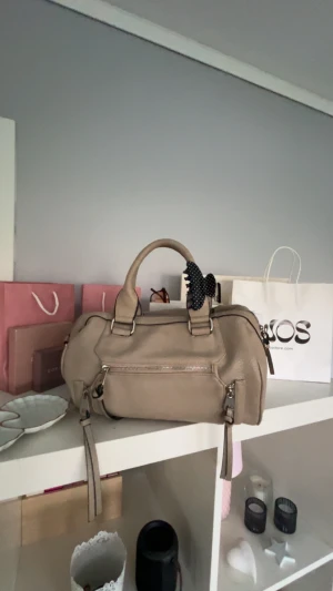 Handväska💗💗 - Snygg beige handväska med två rejäla handtag och flera dragkedjor framtill. Väskan är tillverkad i syntetmaterial med en lätt strukturerad yta och har praktiska fack inuti. Perfekt storlek för allt du behöver och stilren look. De är en gammal modell från Åhléns som ej säljs länge och är svår o få tag på. Priset går alltid att diskutera!!💗💗💘💘💝💝💖💖