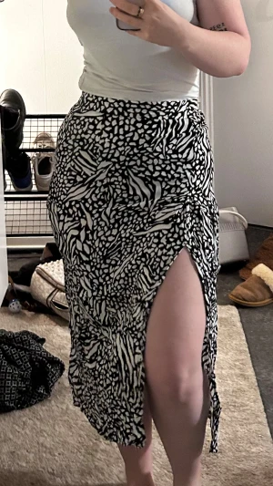 Svartvit långkjol med slits och zebramönster - Säljer en svartvit långkjol med zebramönster och prickar. Kjolen har en hög midja och en snygg slits på sidan som ger en trendig vibe. Materialet känns lätt och flowy, perfekt för dig som gillar att sticka ut med mönster.