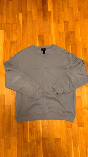 Grå relaxed fit sweatshirt från H&M - Säljer en enkel och stilren grå sweatshirt från H&M i relaxed fit. Tröjan har rund hals, långa ärmar och ribbade muddar vid ärmslut och nederkant. Mjuk insida i fleece som gör den extra skön att ha på sig. Perfekt för chill dagar.