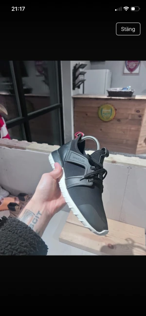 Svarta sneakers från Moncler - Snygga svarta sneakers från Moncler med vit sula och svarta snören. Skorna har Moncler-logga bak och en cool detalj med röd, vit och blå rem baktill. Ovandelen är i syntet och skinn, med en sportig och modern look.