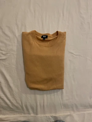 Orange stickad tröja från Uniqlo - Snygg orange stickad tröja från Uniqlo i storlek S. Tröjan är tillverkad i 100% ull och har en klassisk rund halsringning samt långa ärmar. Perfekt för dig som gillar enkel och stilren design med mjukt material.