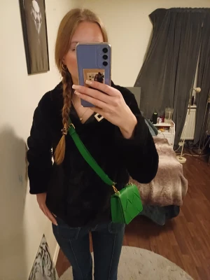 Grön axelväska  - Säljer en snygg grön axelväska med bred band. Väskan har guldfärgade metalldetalj. Perfekt storlek för det viktigaste och ger en poppig färg till din outfit.