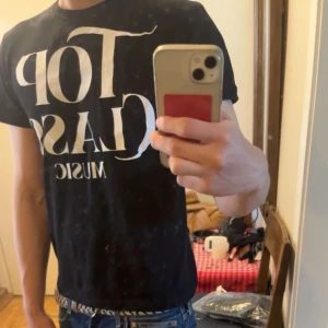 Svart Top Class Music t-shirt - Svart t-shirt med stor vit text 'Top Class Music' på framsidan. Klassisk rund hals och korta ärmar. Passformen är normal och materialet känns som mjuk bomull, perfekt för dig som gillar musik och vill ha en enkel, stilren look.
