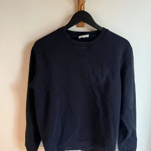 Mörkblå sweatshirt med broderat W - Säljer en mörkblå sweatshirt med broderat W på bröstet. Tröjan har rund halsringning och långa ärmar. Tillverkad i mjuk bomull, perfekt för chill dagar eller när du vill ha en clean look.
