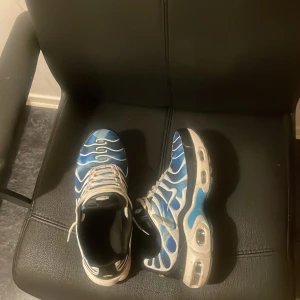 Nike Air Max blå och vita sneakers - Nike Air Max sneakers i blått och vitt med vågiga mönster och vita detaljer. Skorna har synlig Air Max-sula, snörning och rund tå. Materialet är syntet och skinn, med en cool design som sticker ut. Perfekt för dig som gillar streetwear och sportig stil.