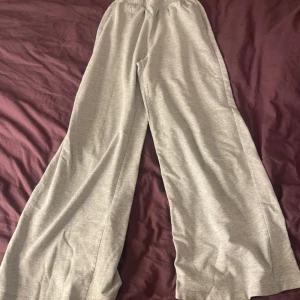Grå wide mjukisbyxor H&M Divided XS - Gråa mjukisbyxor från H&M Divided i storlek XS. Byxorna har bred resår i midjan och är i en loose, wide modell med raka, vida ben. Tillverkade i mjuk bomullsblandning med polyester för extra komfort. Perfekta för chill dagar eller när du vill vara extra bekväm. En svart fläck av franslim på byxorna.
