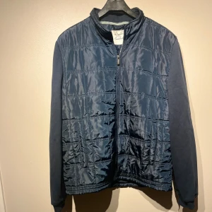 Mörkblå Cardigan  - Snygg mörkblå quiltad jacka från Tchibo Essentials. Jackan har dragkedja framtill, diskret rutmönster och är tillverkad i ett lätt och smidigt syntetmaterial. Perfekt för dig som gillar stilren och enkel design.