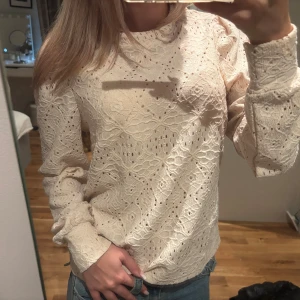 Beige spetsblus med lång ärm - Säljer en beige blus med lång ärm och vackert spetsmönster. Blusen har en rund halsringning och är tillverkad i ett lätt, luftigt material med broderade detaljer. Perfekt för dig som gillar romantisk och feminin stil.