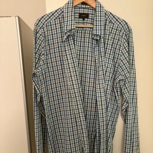 Rutig blå och vit skjorta från boomerang - Snygg rutig skjorta från boomerang i blått och vitt med klassisk krage och långa ärmar. Skjortan har knappar framtill och är gjord i mjuk bomull som känns skön mot huden. Perfekt för dig som gillar en chill och stilren look.