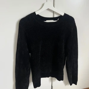 Svart stickad tröja från Sandro Paris - Svart stickad tröja från Sandro Paris med snyggt texturerat mönster på framsidan och släta ärmar. Rund halsringning och långärmad modell som ger en clean och stilren vibe. Perfekt för dig som gillar klassiska plagg med en twist.
