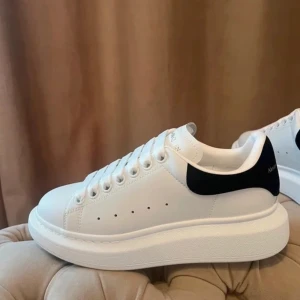 Alexander McQueen vita sneakers strl 38 - Säljer ett par ikoniska vita Alexander McQueen sneakers med svart hälflik och guldfärgad logga. Skorna har chunky plattformssula, rund tå och klassisk snörning. Tillverkade i skinn med stilren design som lyfter varje outfit.
