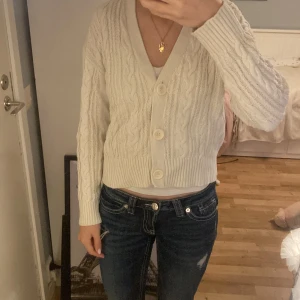 Vit kabelstickad kofta från Lindex - Supermysig vit kabelstickad kofta från Lindex med stora knappar framtill och v-ringning. Koftan är mysig och perfekt att slänga över ett linne eller t-shirt för en chill look.