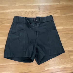 Svarta shorts med bälte - Snygga svarta shorts med  brett bälte med spänne. Shortsen har markerade sömmar och stora fickor framtill. 