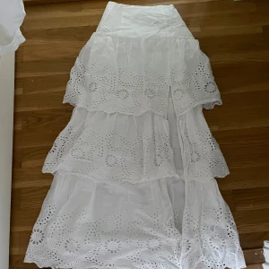 Vit långkjol med broderade volanger - Superfin vit långkjol med flera lager volanger och broderade detaljer. Kjolen har ett romantiskt hålmönster och ger en luftig känsla. 